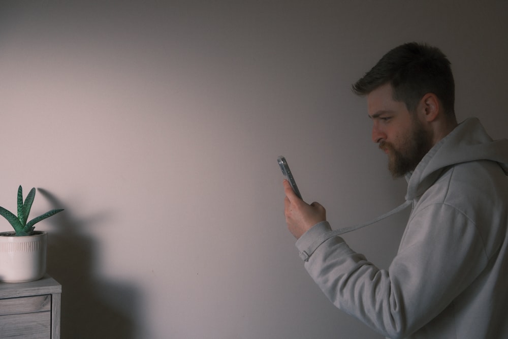 a man holding a cell phone next to a plant