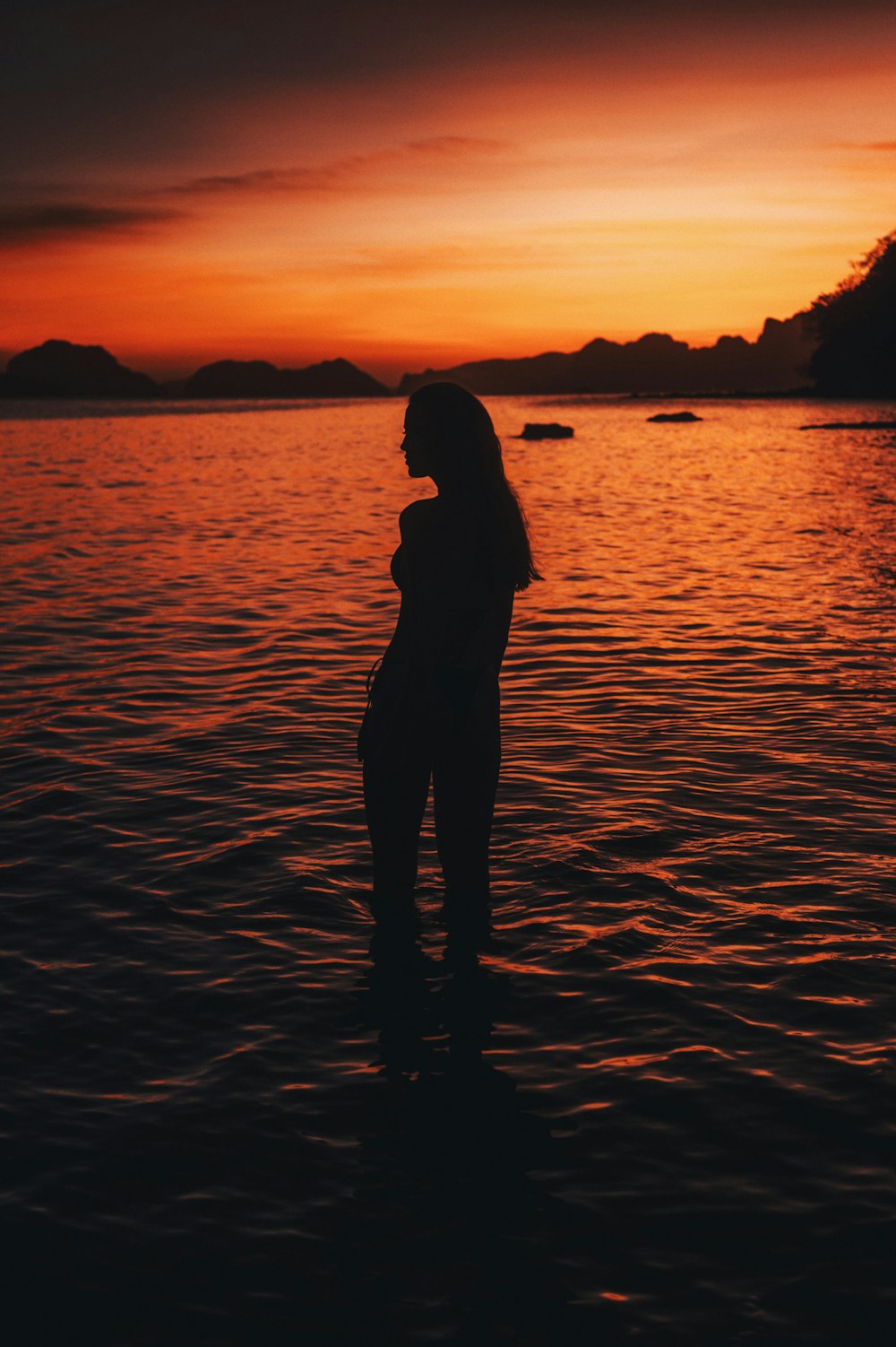 a woman standing in the water at sunset