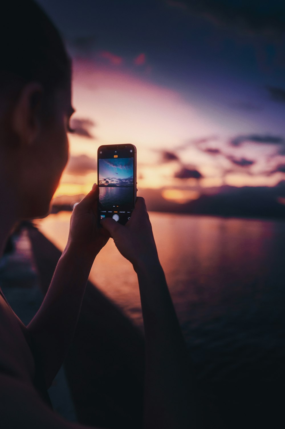 uma mulher tirando uma foto de um pôr do sol com seu celular