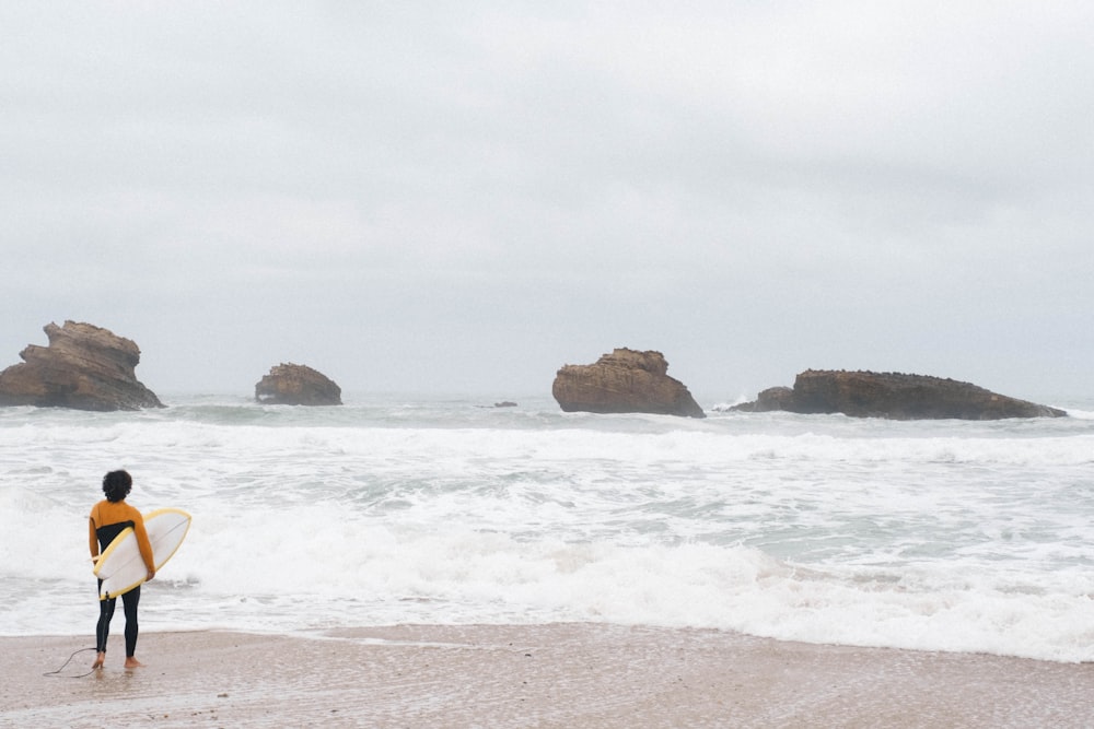 um homem segurando uma prancha de surf em cima de uma praia de areia