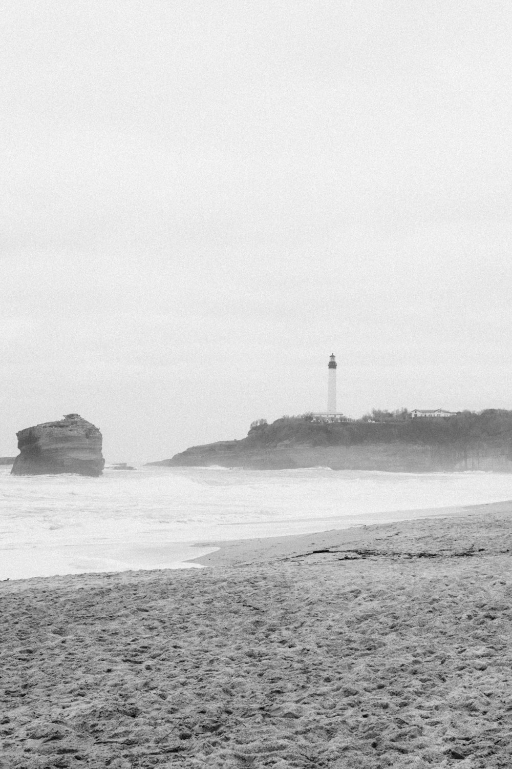 a black and white photo of a beach with a lighthouse in the background