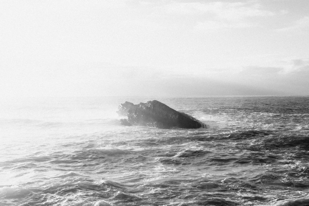 a black and white photo of a rock in the middle of the ocean
