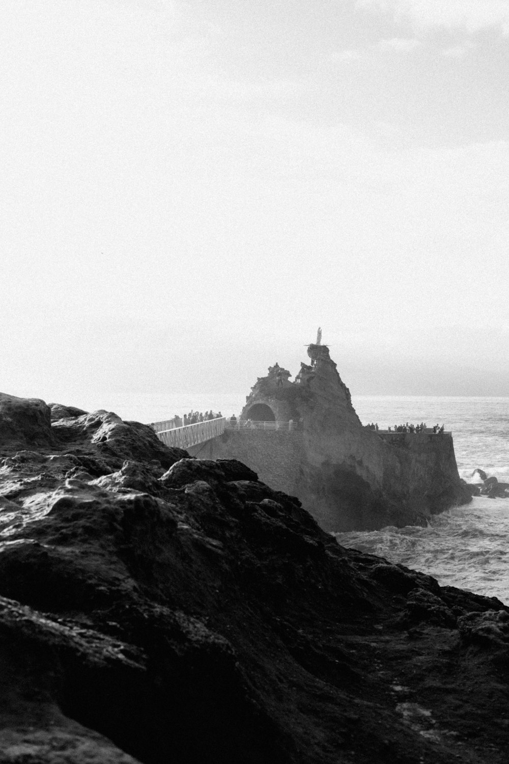 a black and white photo of a lighthouse on a rocky shore