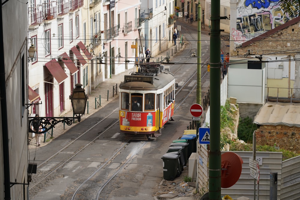 a yellow and red trolley traveling down a street next to tall buildings
