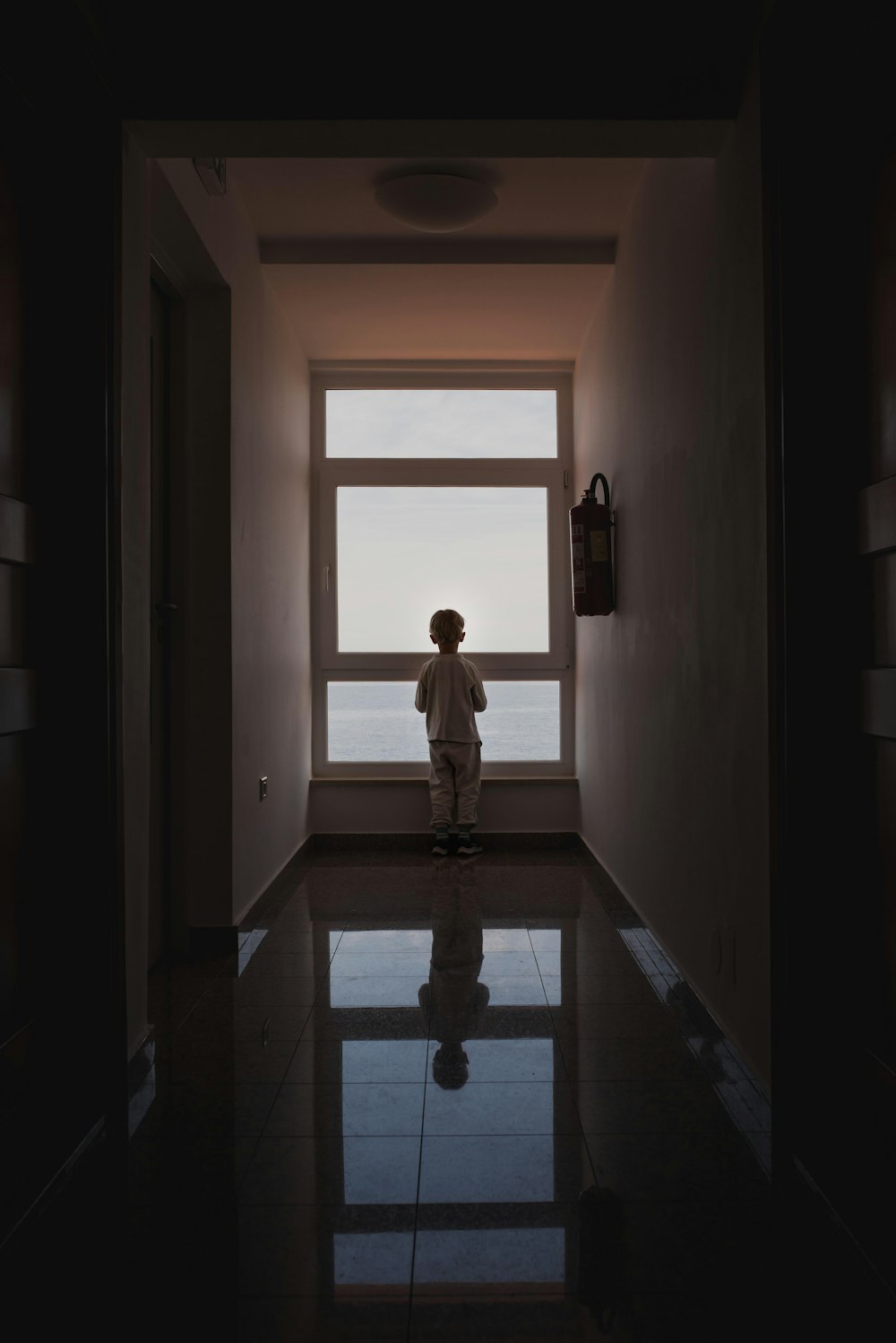 une personne debout dans un couloir sombre regardant par la fenêtre