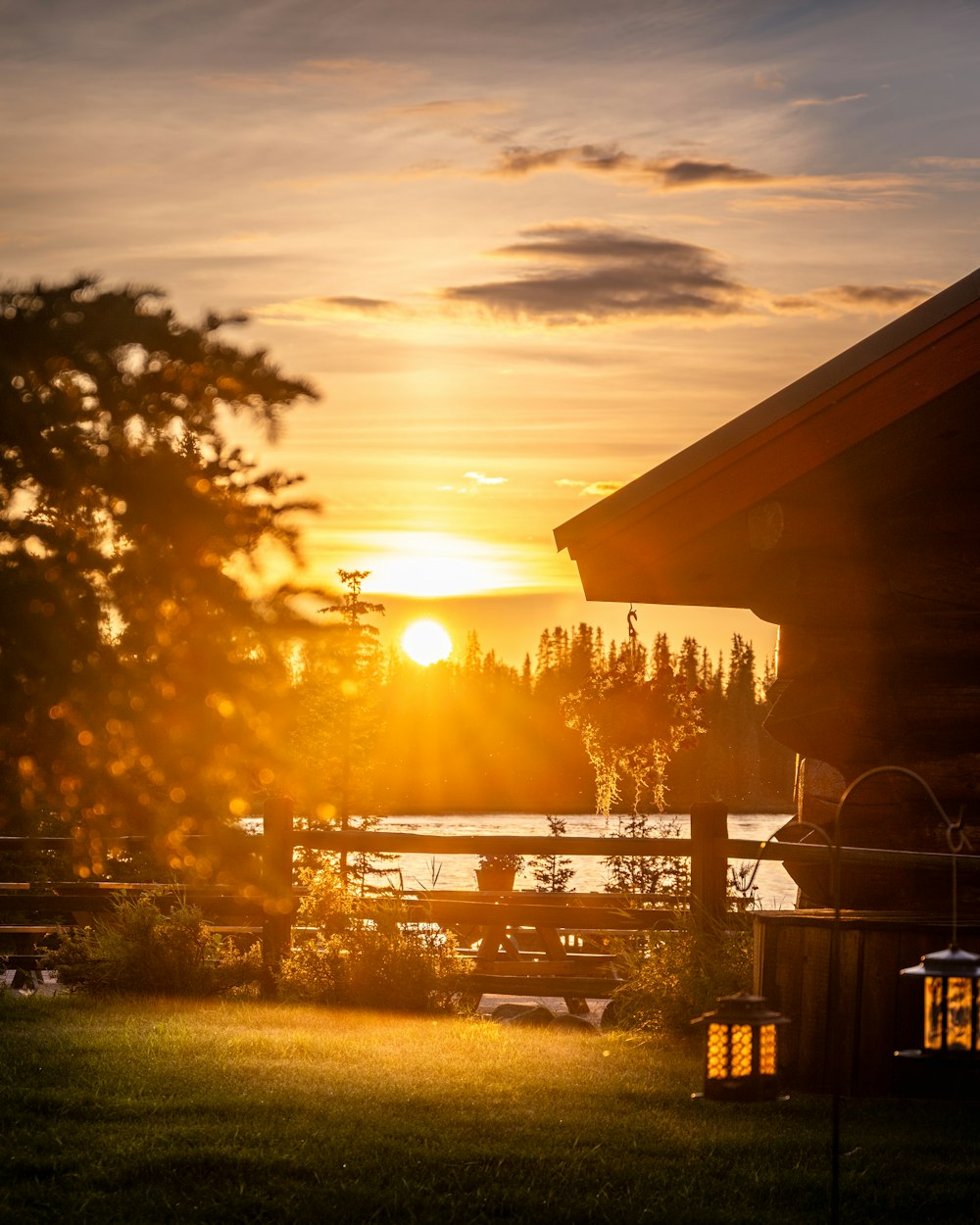 the sun is setting over a lake and a cabin