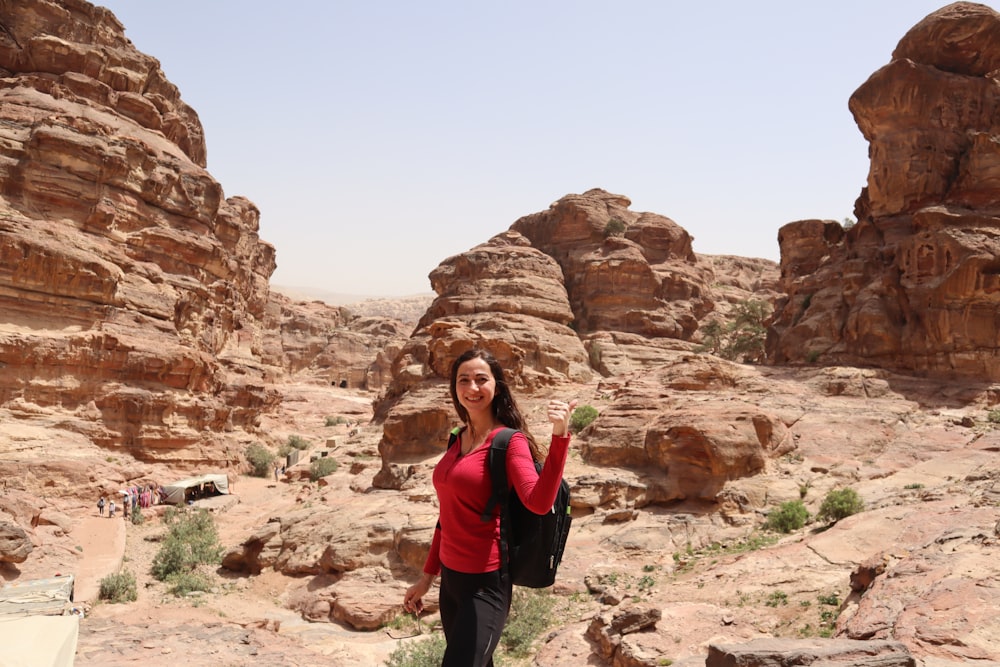 a woman in a red shirt and black pants standing in the desert