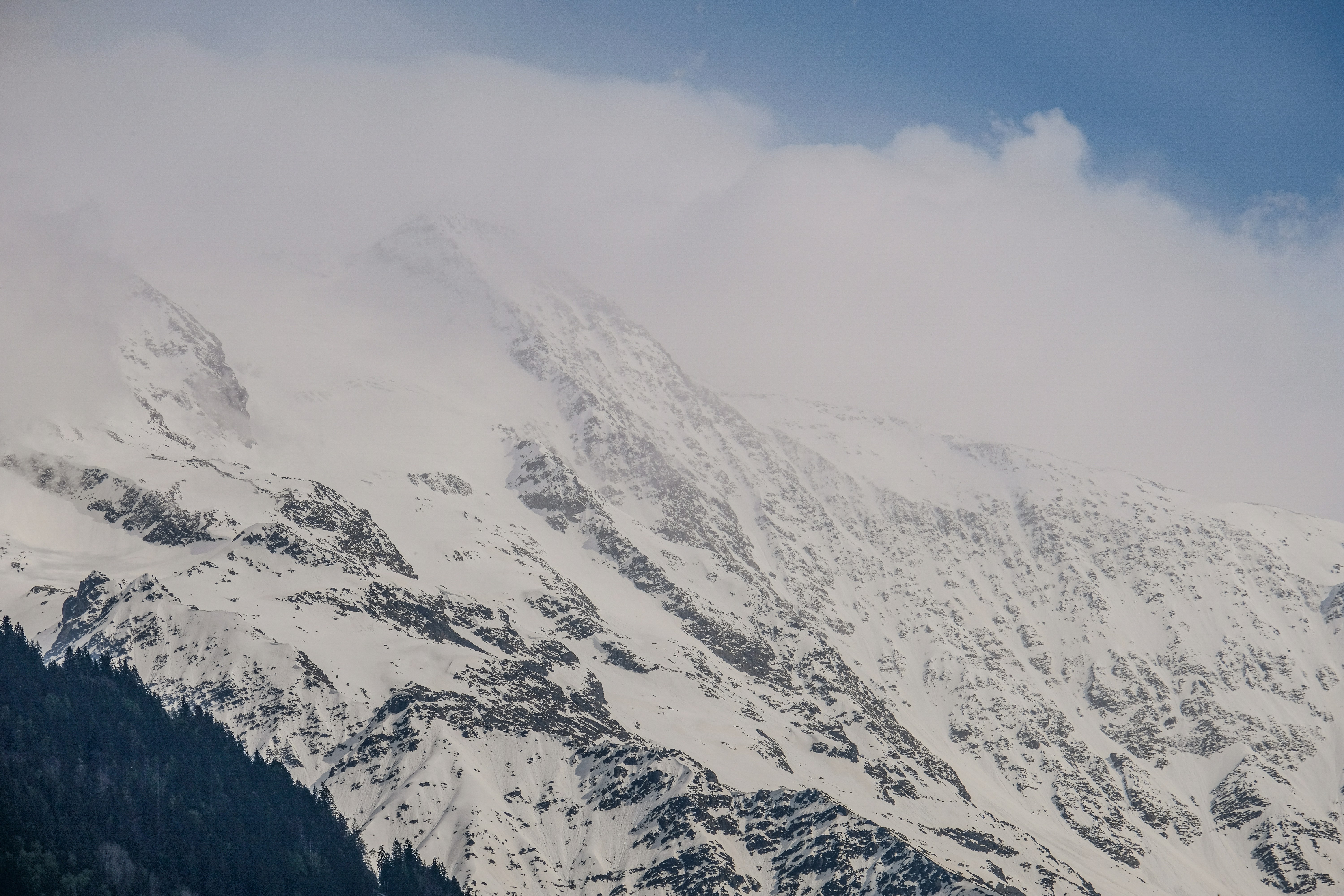 a mountain covered in snow and clouds under a blue sky