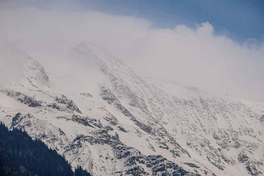 a mountain covered in snow and clouds under a blue sky