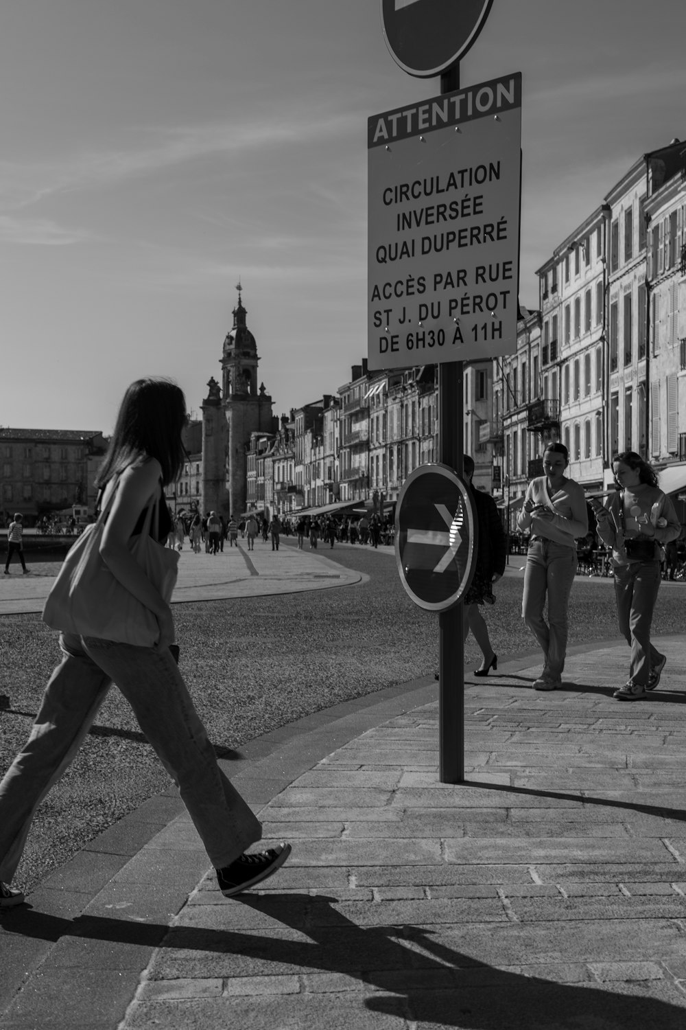 a woman walking down a sidewalk next to a street sign