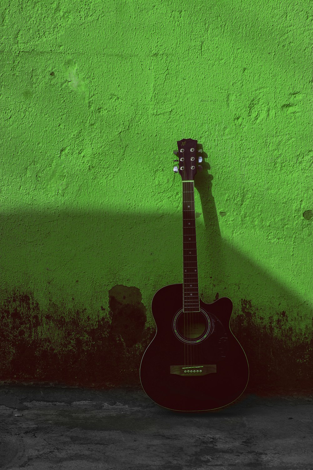 a black guitar leaning against a green wall