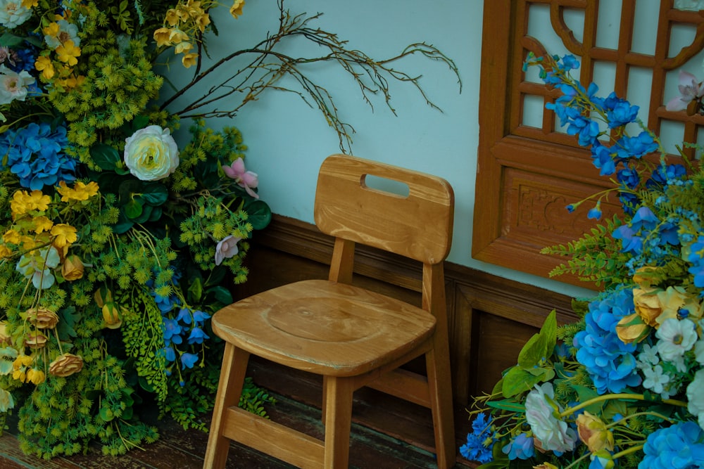 a wooden chair sitting in front of a wall of flowers