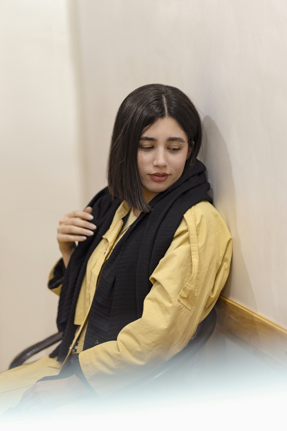 a woman leaning against a wall wearing a scarf