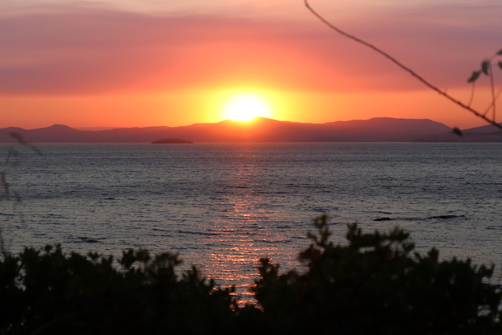 the sun is setting over the ocean with mountains in the distance