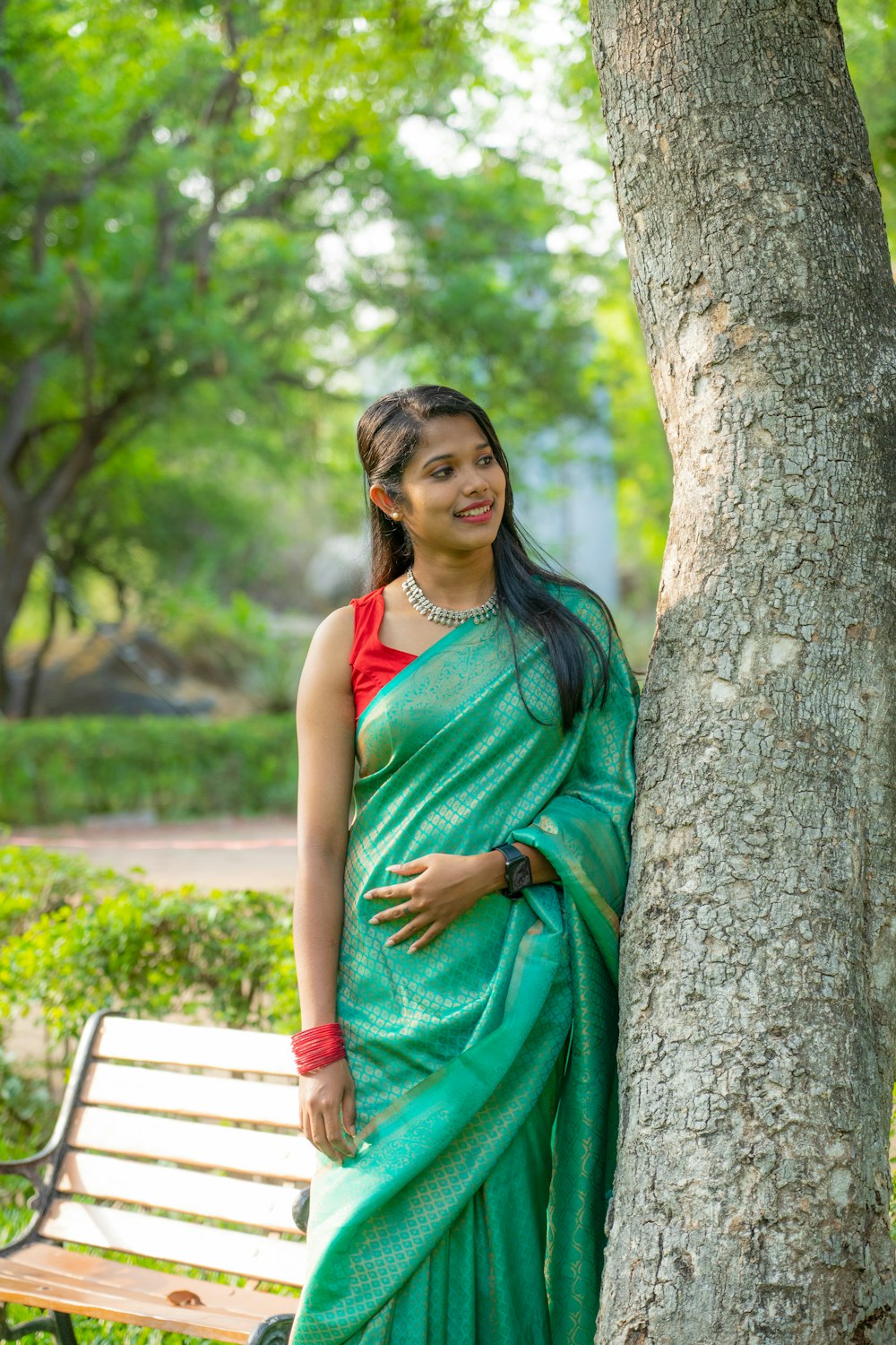 a woman in a green sari leaning against a tree