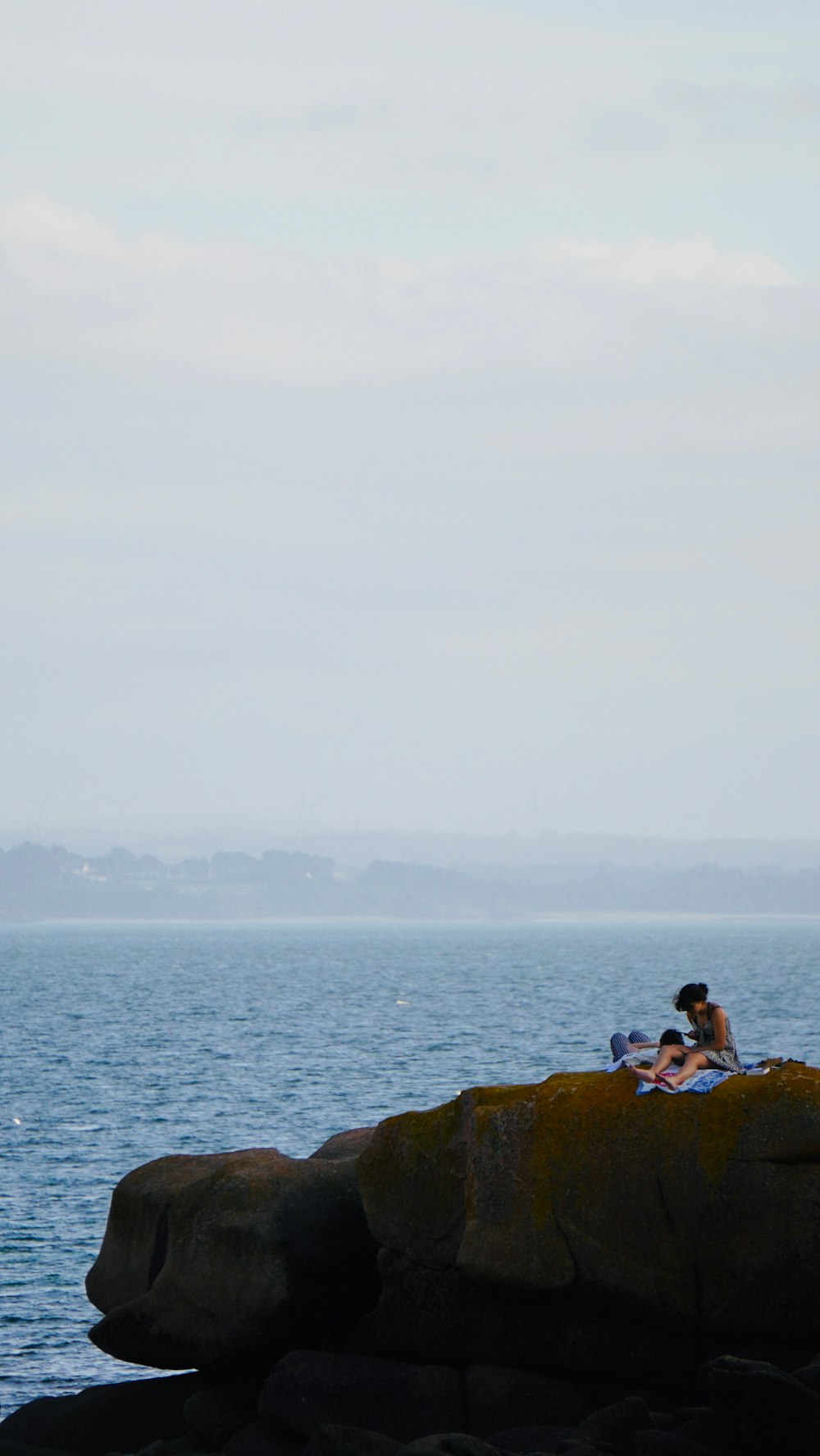 two people sitting on a rock near the ocean