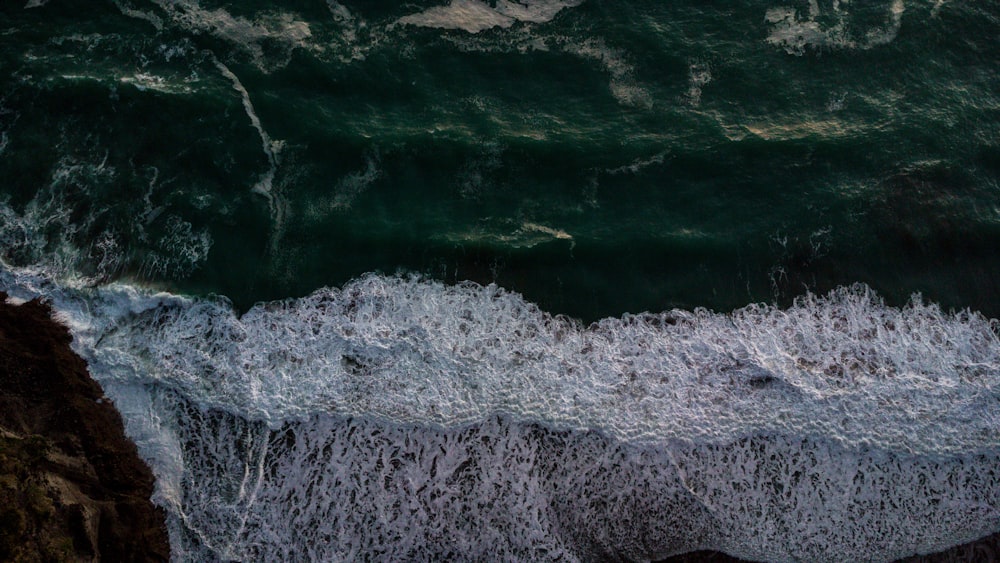 an aerial view of the ocean with waves crashing on the rocks