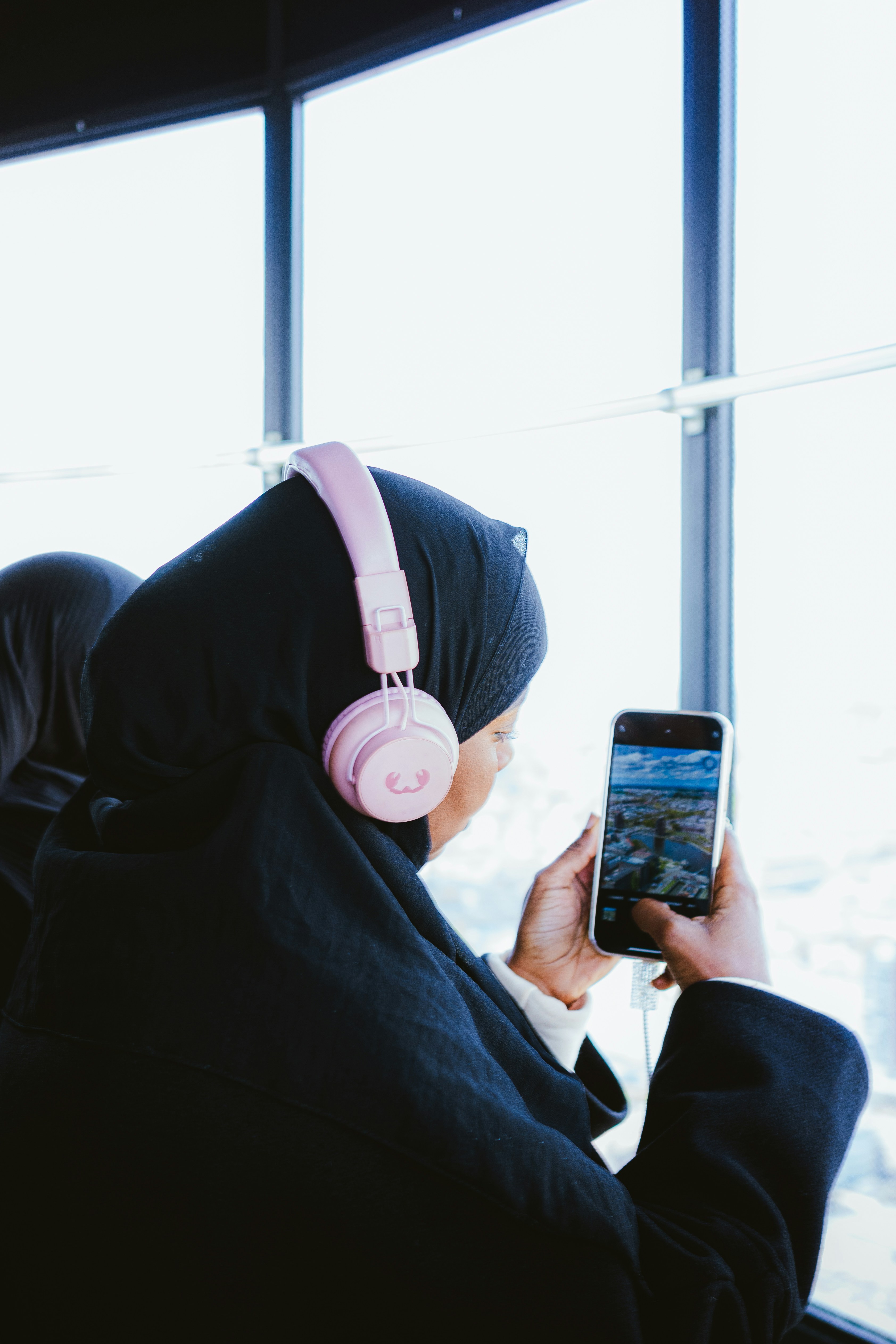 Woman in hijab looking at her phone by a window.