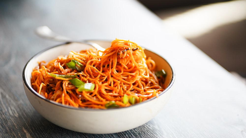 a white bowl filled with carrot noodles on top of a wooden table