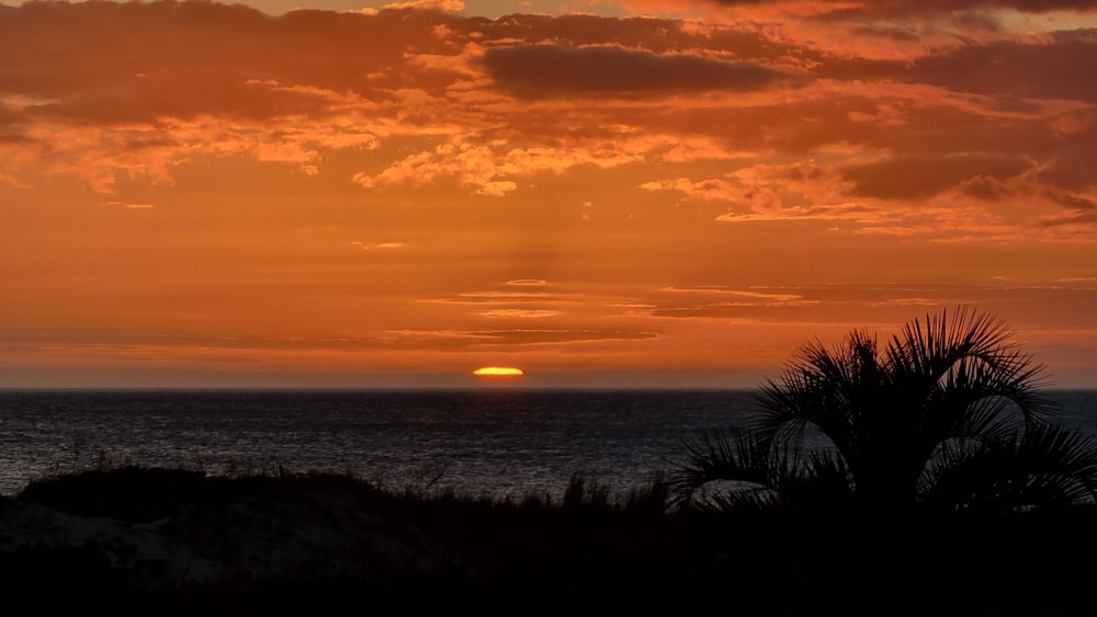 the sun is setting over the ocean on a cloudy day