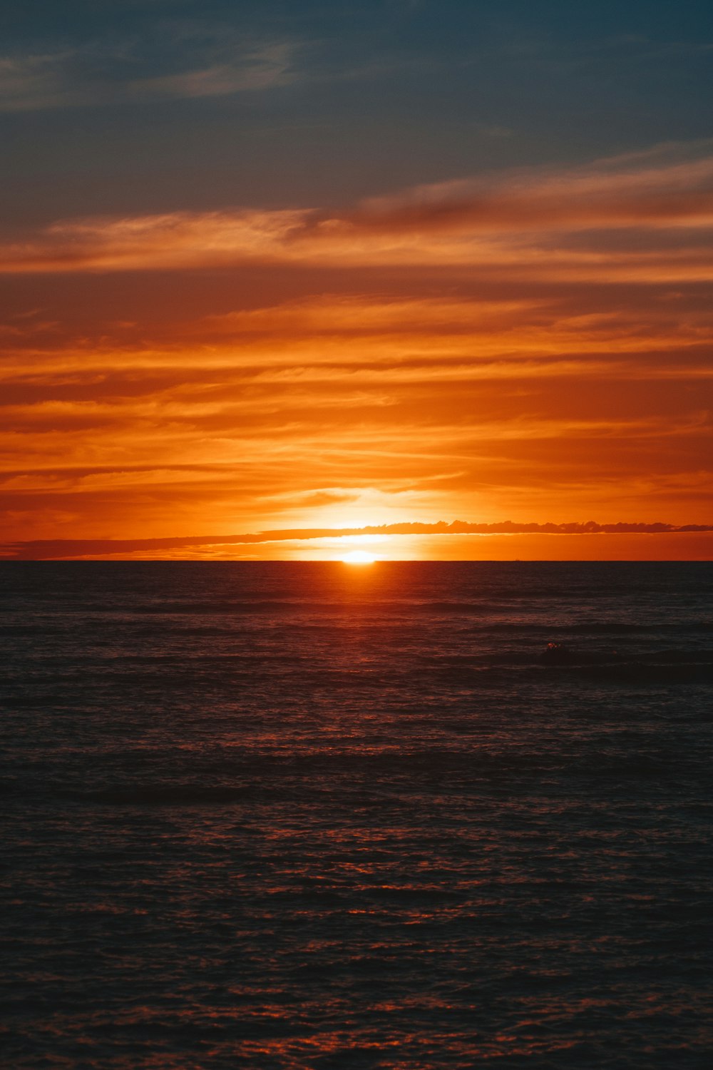 the sun is setting over the ocean with a boat in the water