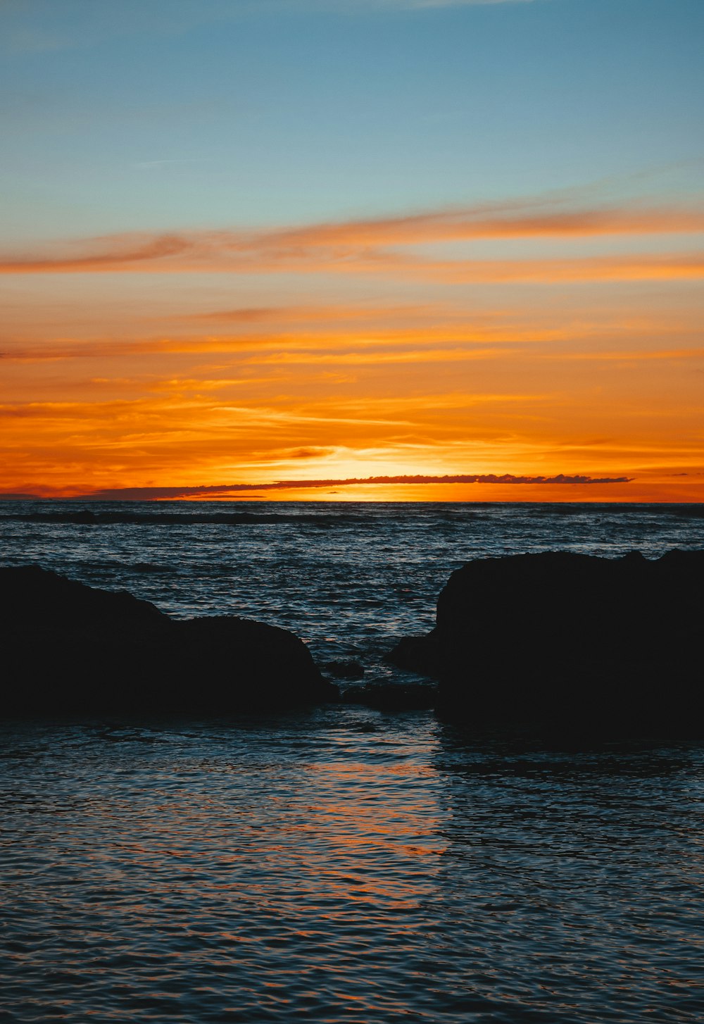 a sunset over a body of water with rocks in the foreground