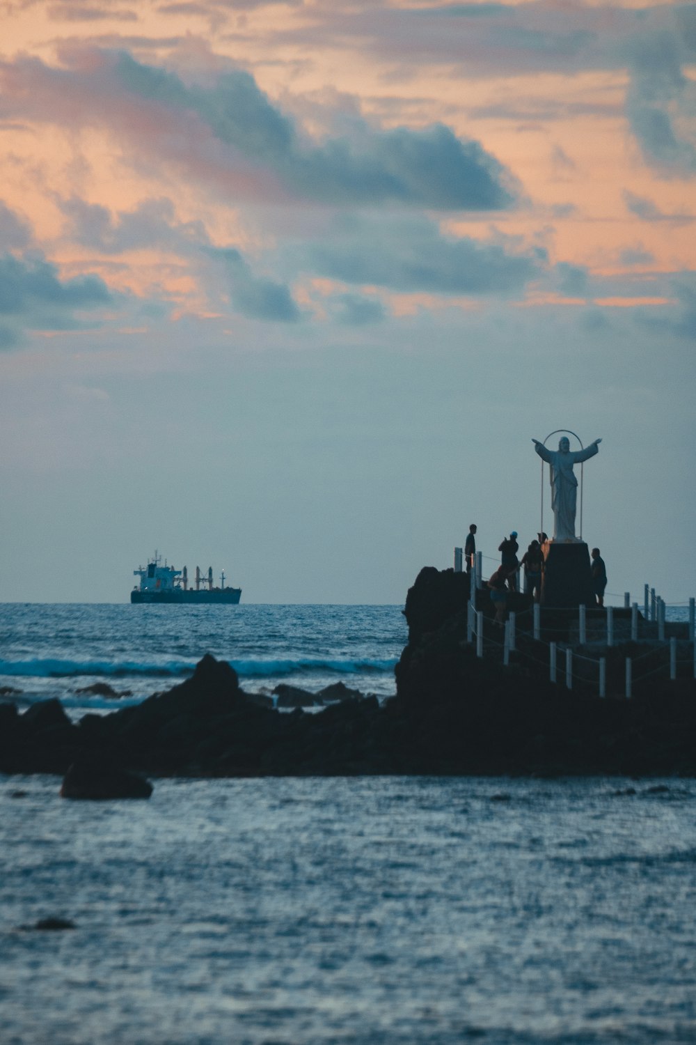 a statue of jesus on top of a rock in the ocean