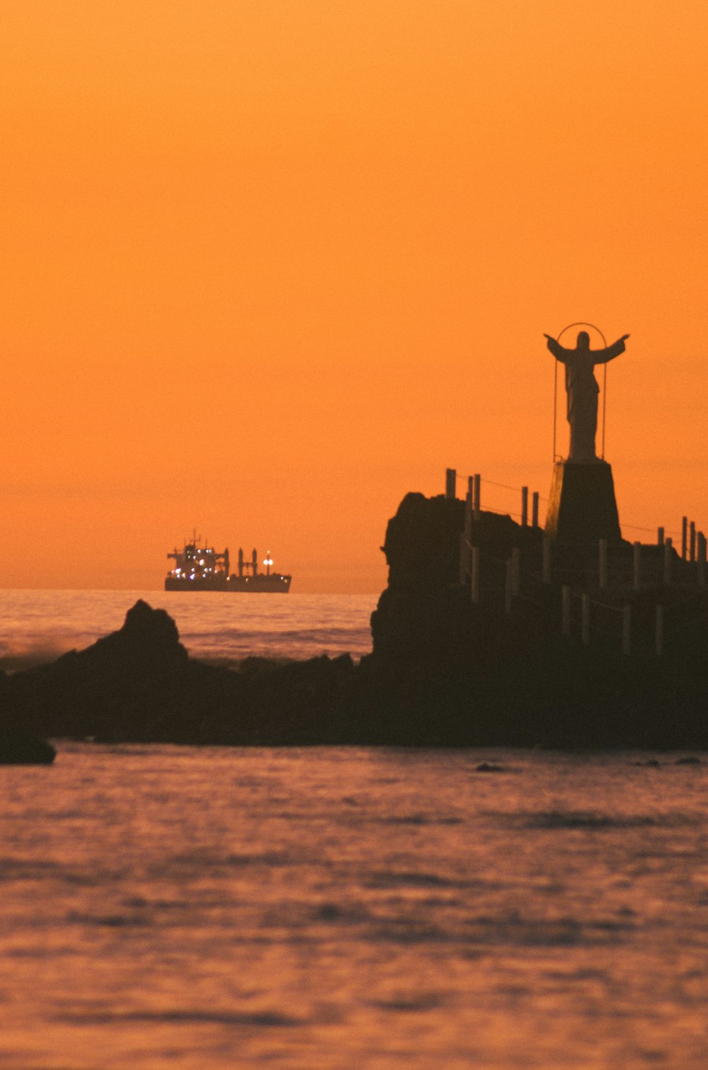 a statue of jesus on top of a rock in the ocean