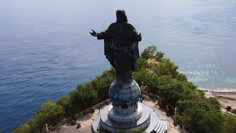 a statue of a man with his arms outstretched in front of a body of water
