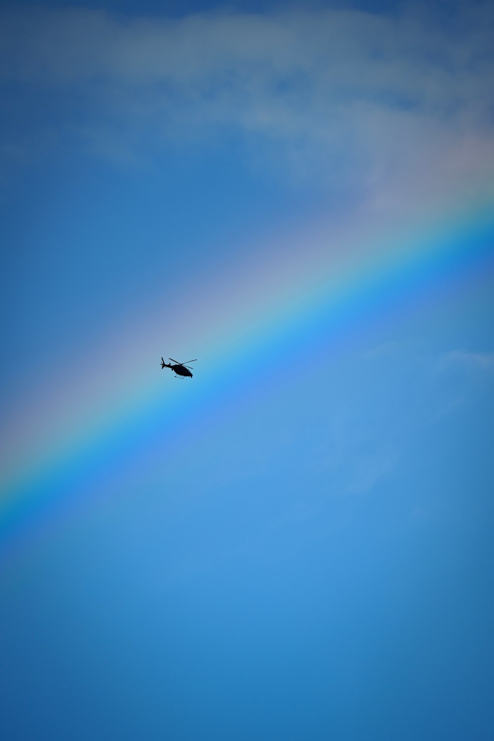 a helicopter flying under a rainbow in the sky