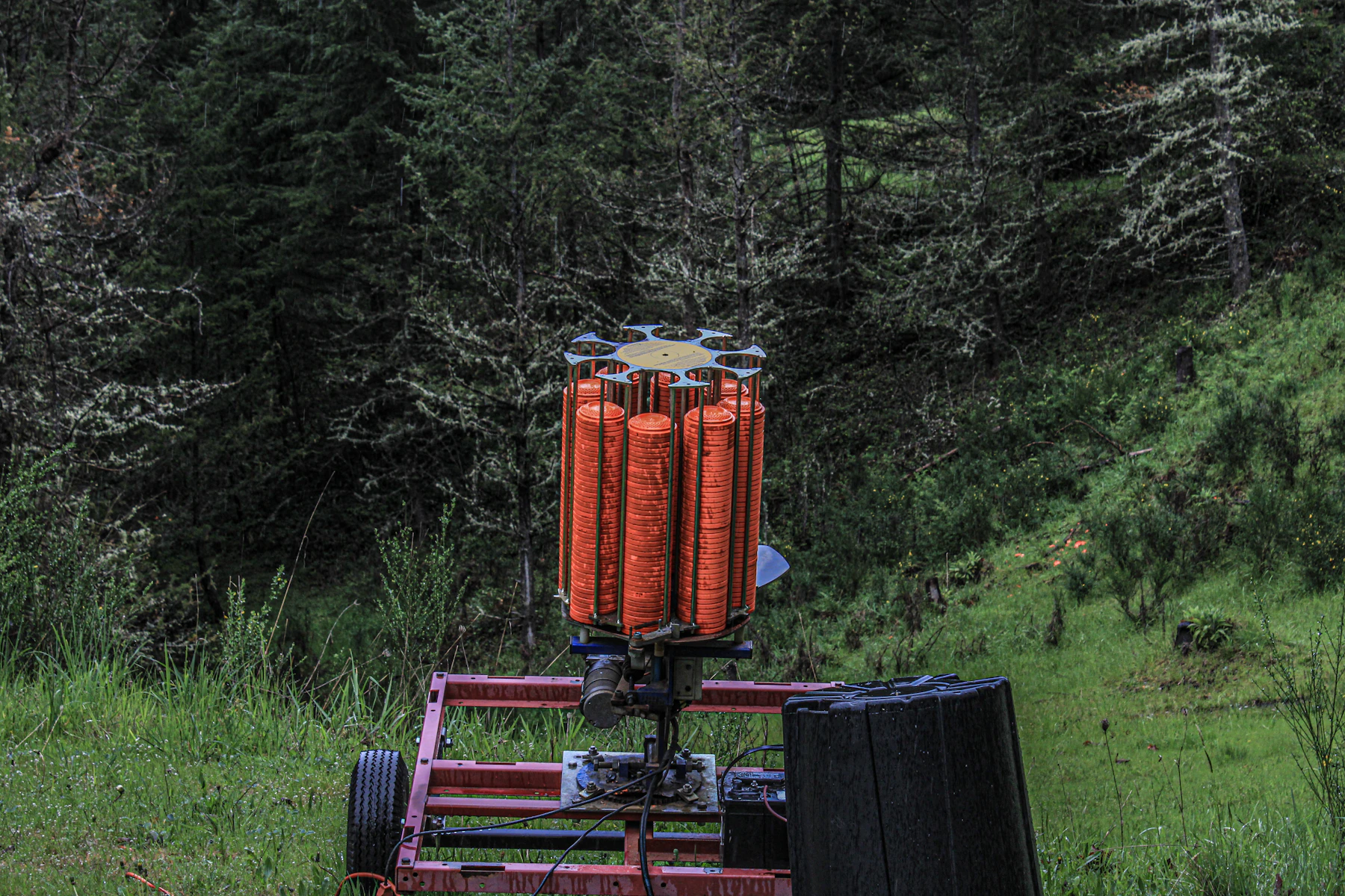A clay trap machine loaded with a stack of orange clays at the edge of a wood