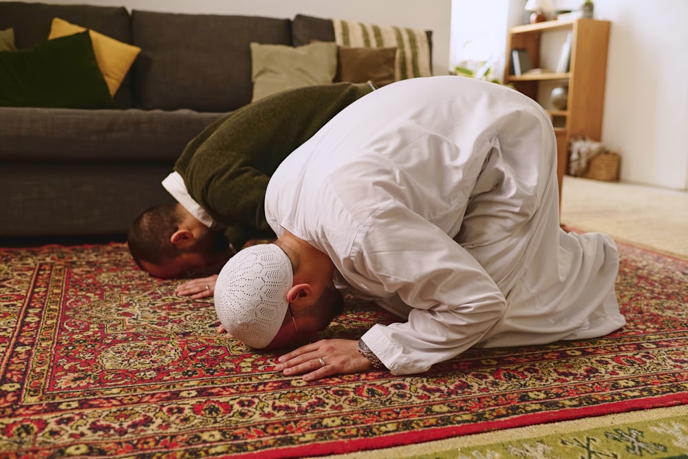 a man in a white outfit is praying on a rug