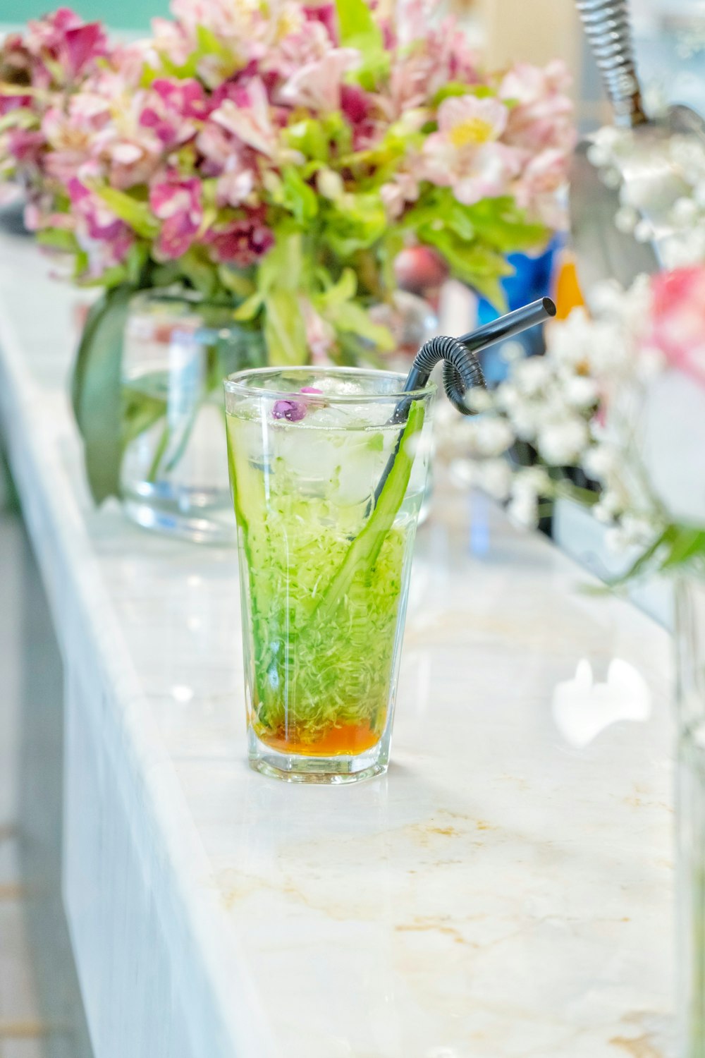 a glass filled with green liquid next to a vase of flowers