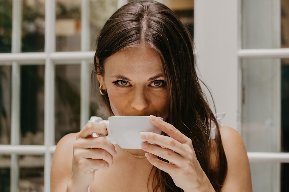 a woman drinking from a cup in front of a window