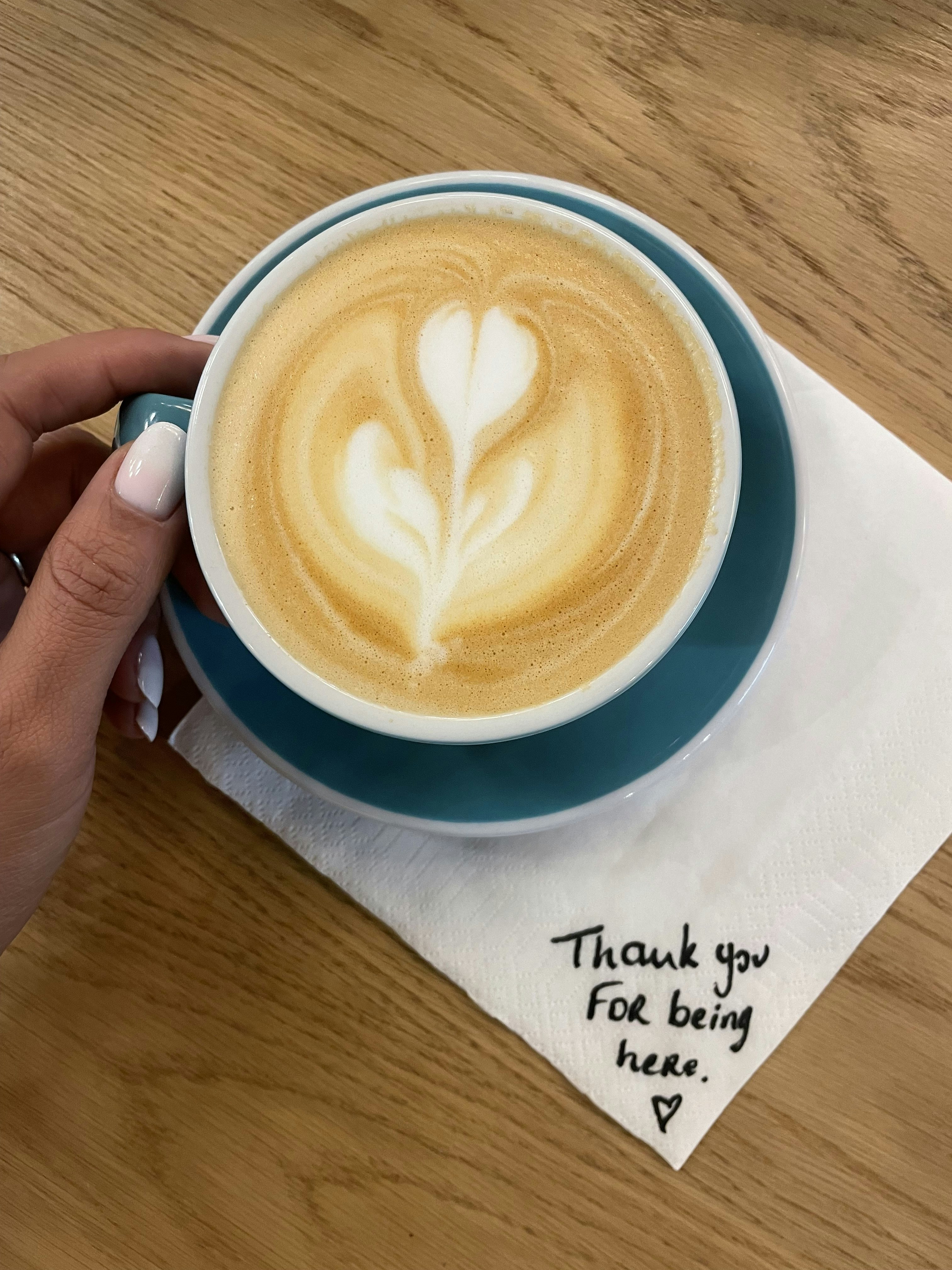 a person holding a cup of coffee on top of a wooden table