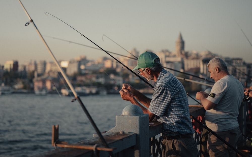 a couple of men standing on top of a pier next to a body of water