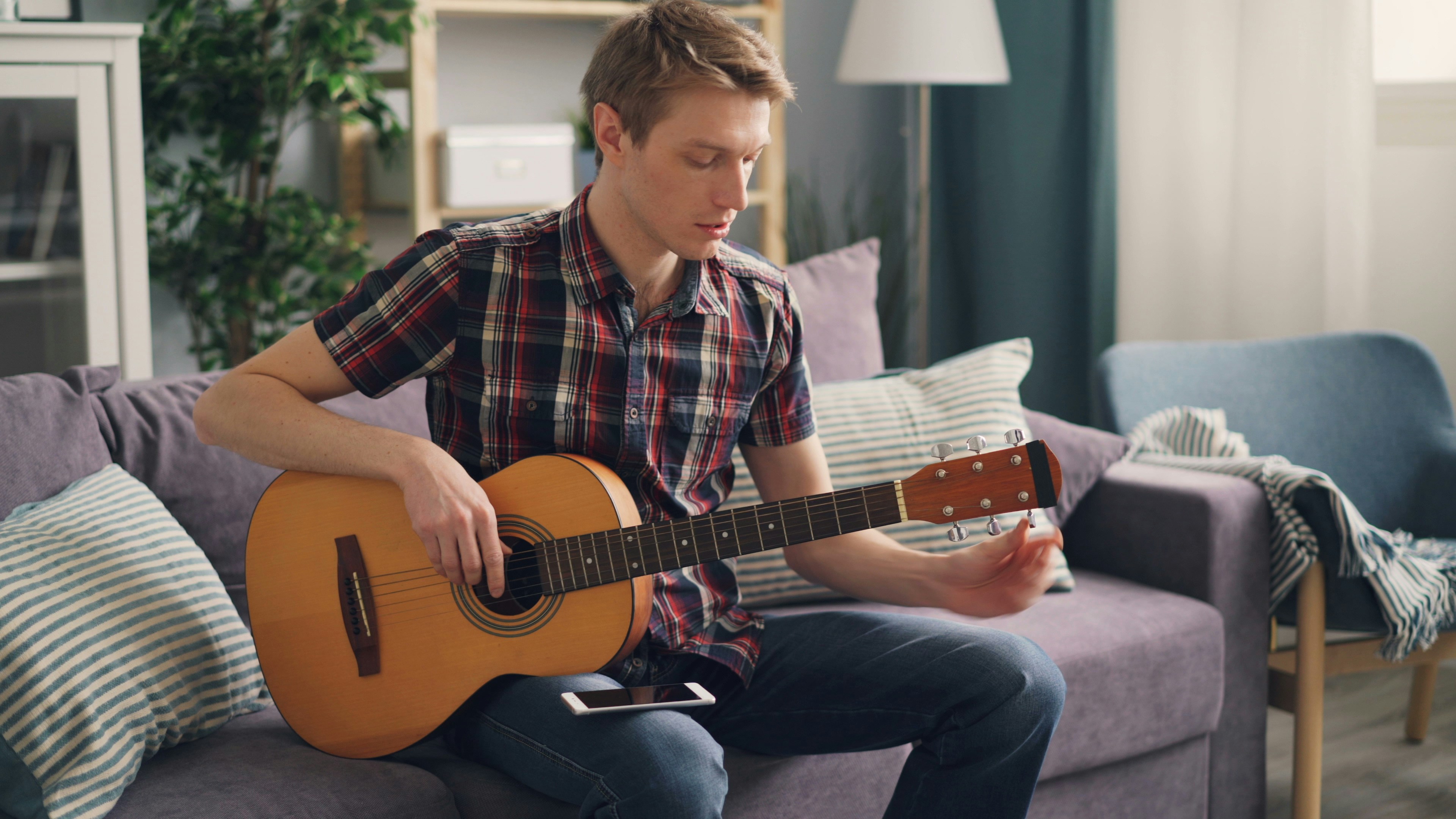 A man sitting on a couch playing a guitar photo – Free Guitar Image on ...