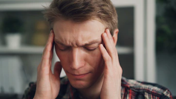 A man with eyes closed holding his temples with both hands