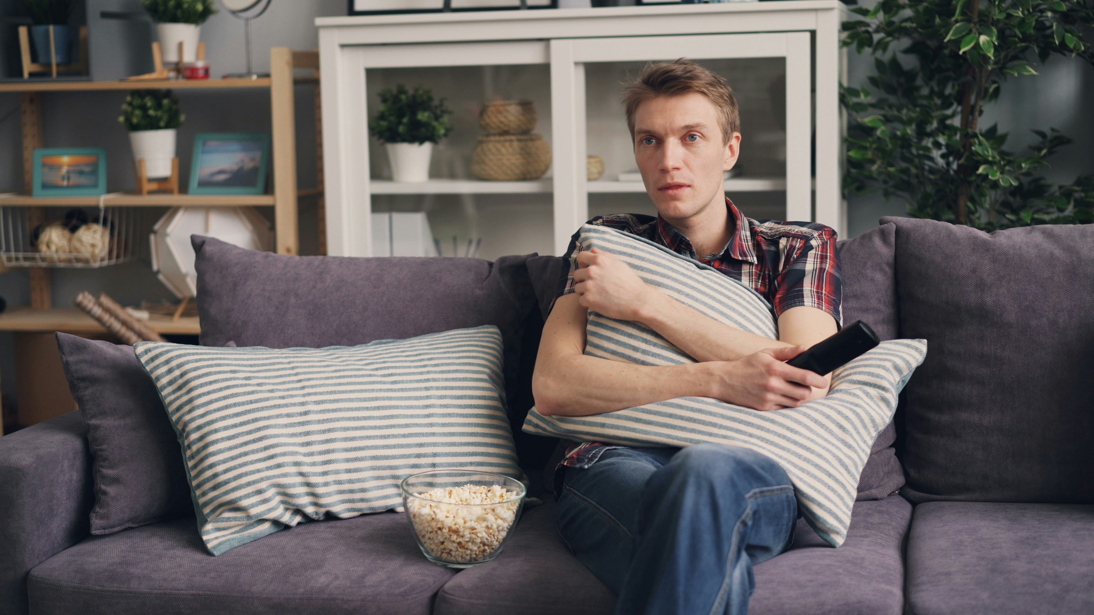 Man sits on a sofa with popcorn and a remote.