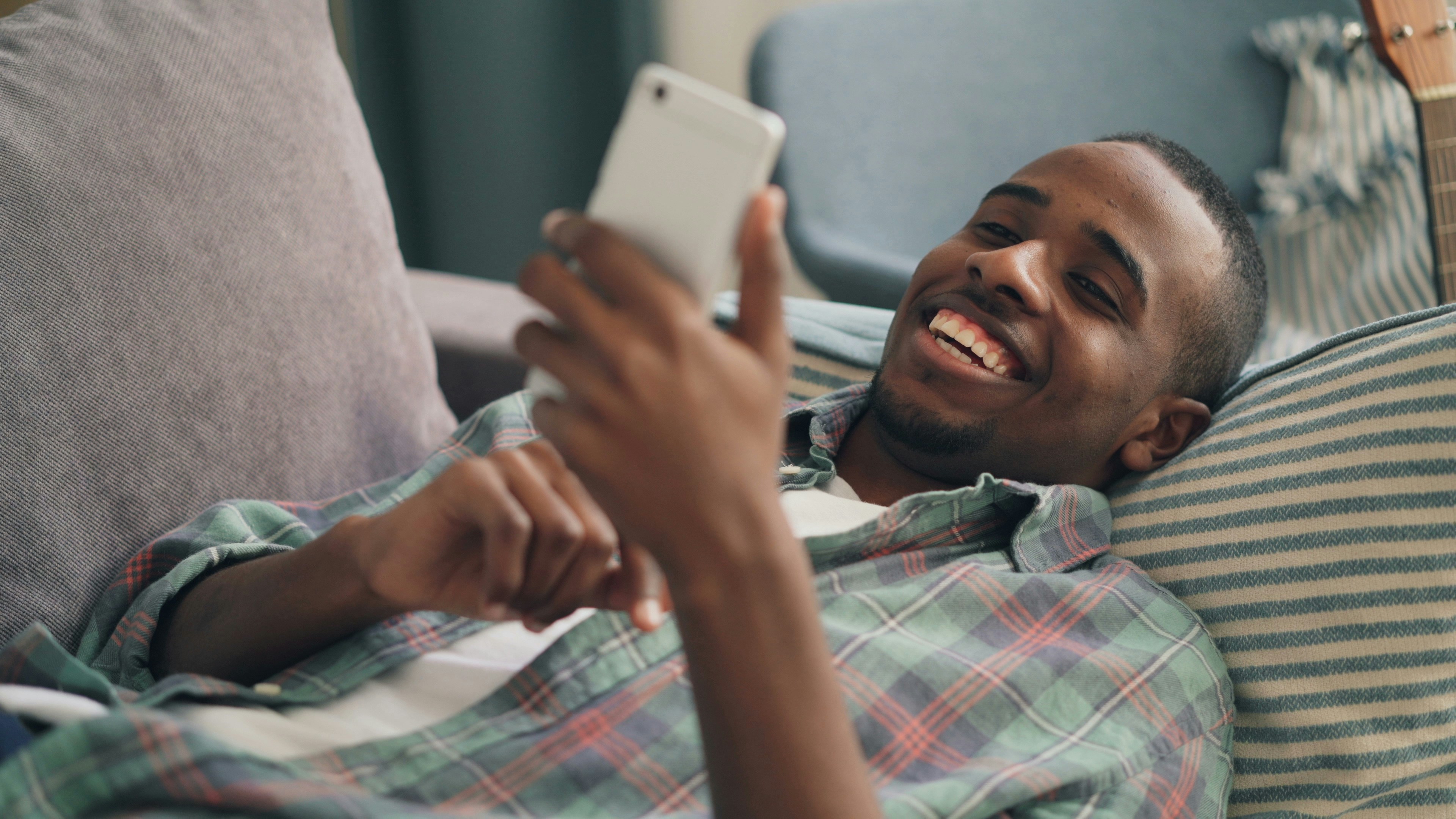 person smiling while reading a message on their phone in a cozy bed.