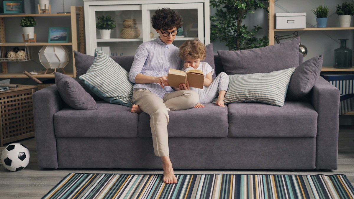 A woman on a couch reading a book to a child, illustrating fun reading activities for children.