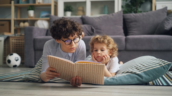 a man and a little girl laying on the floor reading a book