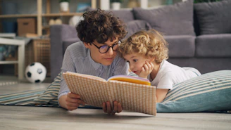 a woman and a child laying on the floor reading a book