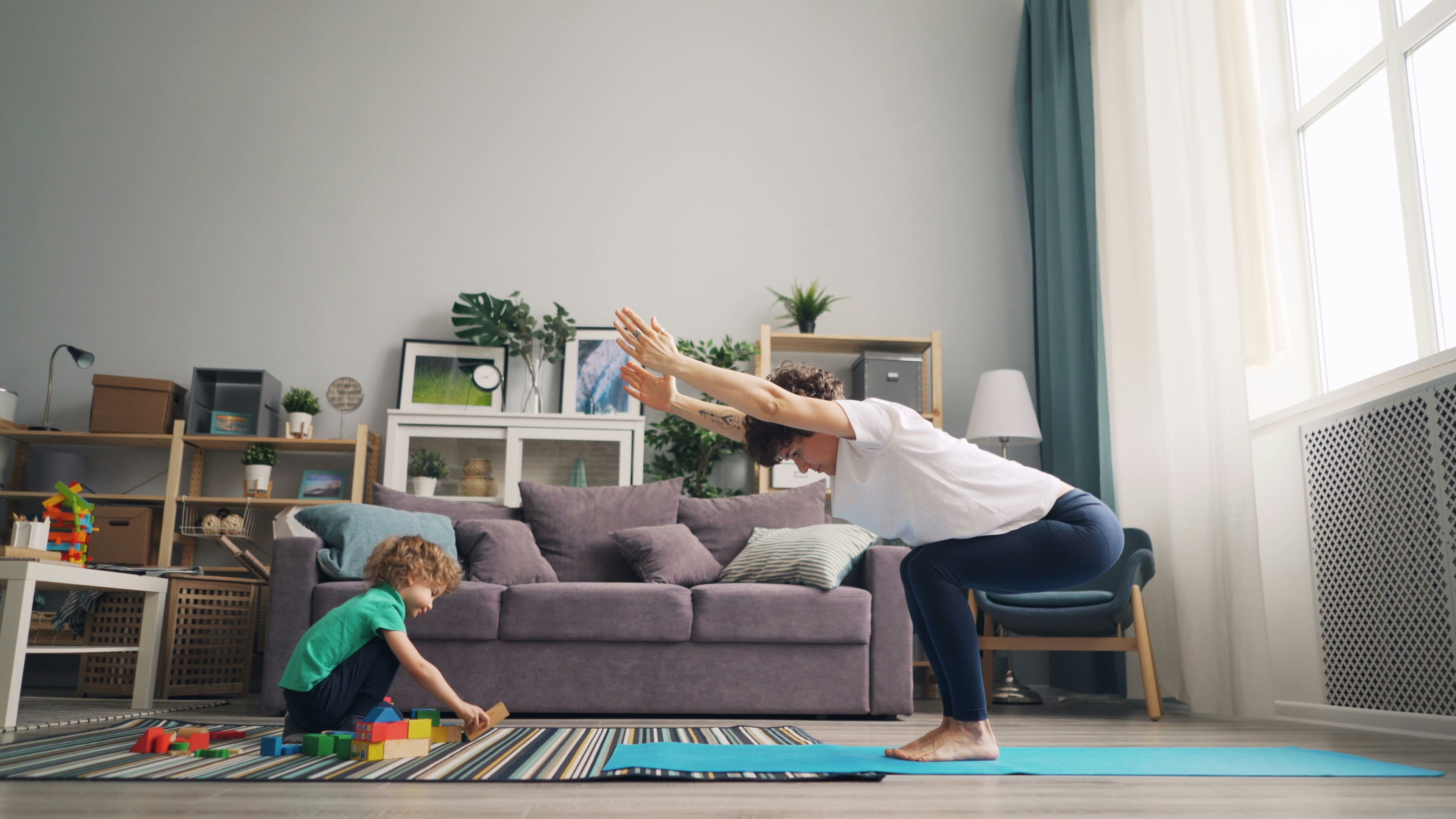 Postpartum mother doing gentle home exercise while child plays in the living room