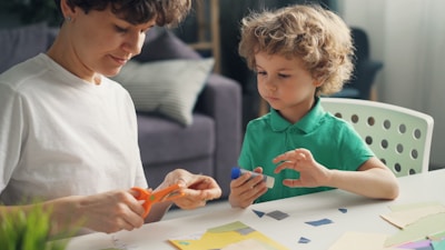 a woman and a child sitting at a table with scissors