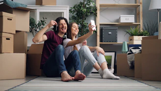 a man and a woman sitting on the floor in a room with moving boxes