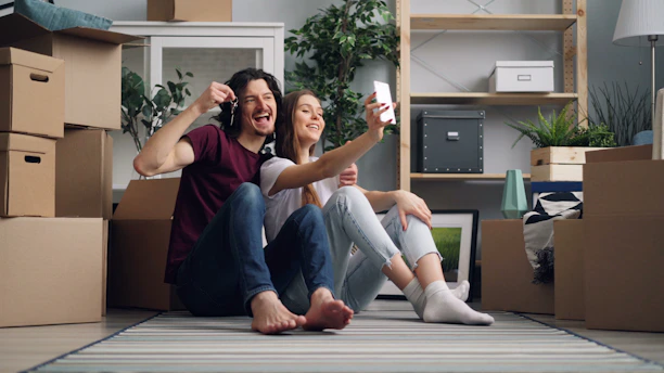 a man and a woman sitting on the floor in a room with moving boxes