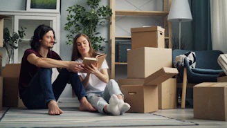 a man and a woman are sitting on the floor surrounded by moving boxes