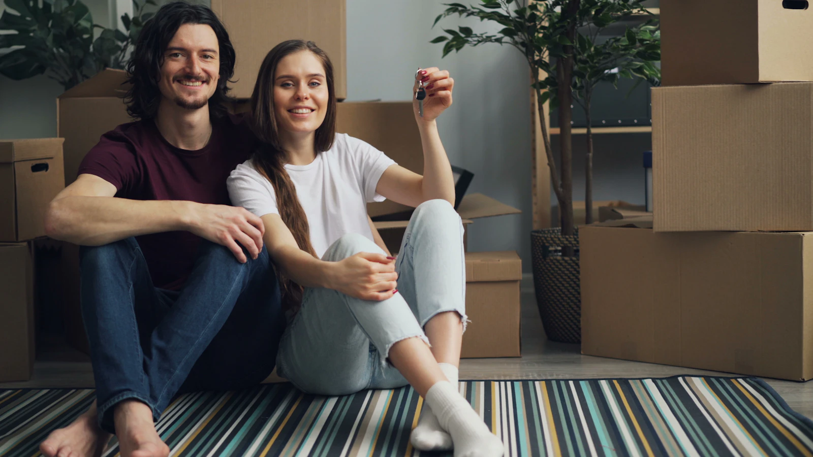 A couple sitting among moving boxes in their new home, holding the keys