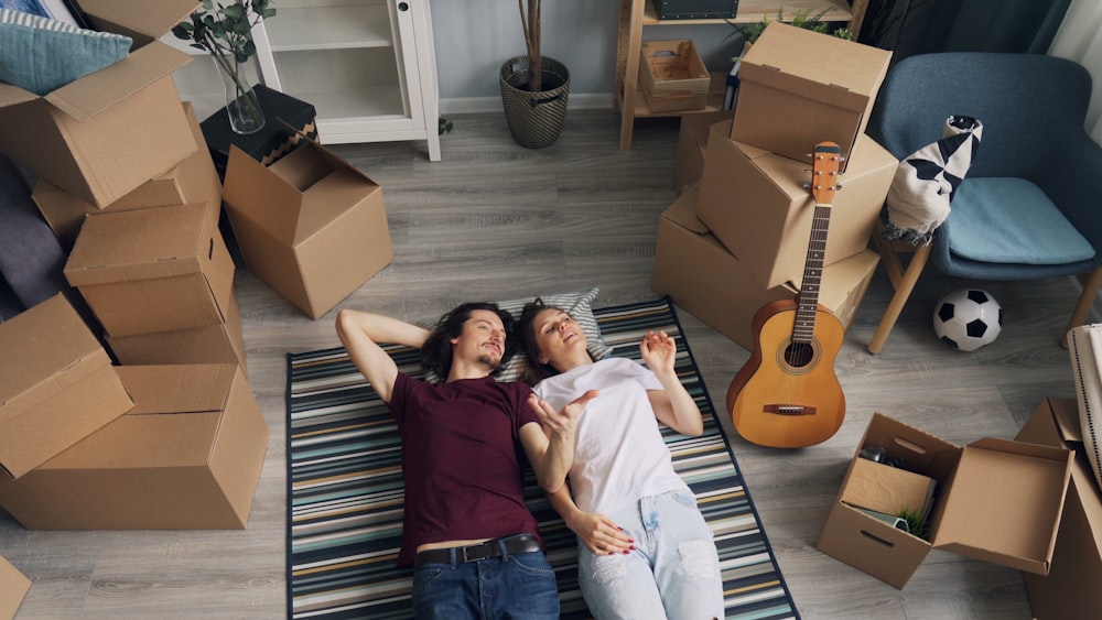 a man and a woman laying on a rug in a room full of moving boxes